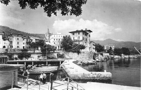 Lovran op een oude ansichtkaart uit de jaren zestig Zwartwitfoto van haventje met huizen eromheen en heuvels erachter